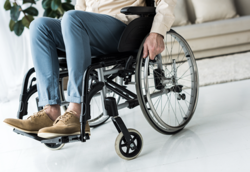 Personne en fauteuil roulant dans un espace intérieur, vêtue de pantalon bleu et chaussures marron.