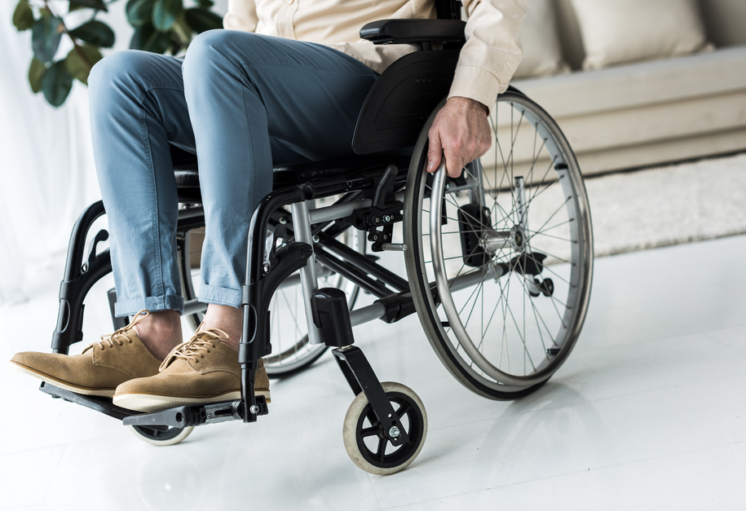 Personne en fauteuil roulant dans un espace intérieur, vêtue de pantalon bleu et chaussures marron.