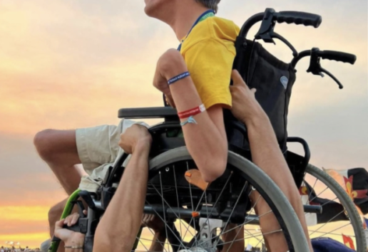 Un athlète en fauteuil de course sportif, entouré de supporters, lève les bras vers le ciel au coucher du soleil.
