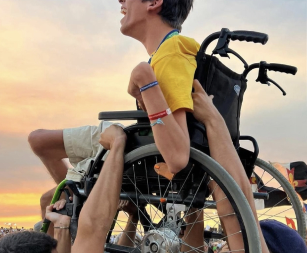 Un athlète en fauteuil de course sportif, entouré de supporters, lève les bras vers le ciel au coucher du soleil.