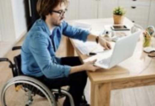 Un homme en fauteuil roulant travaille sur un ordinateur portable dans une cuisine moderne, accompagné d'un petit chien à s