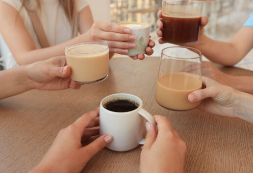 Des mains autour d'une table tenant divers types de boissons chaudes : café, latte et cappuccino.