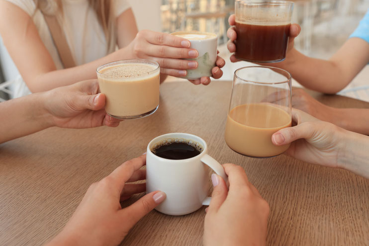 Des mains autour d'une table tenant divers types de boissons chaudes : café, latte et cappuccino.