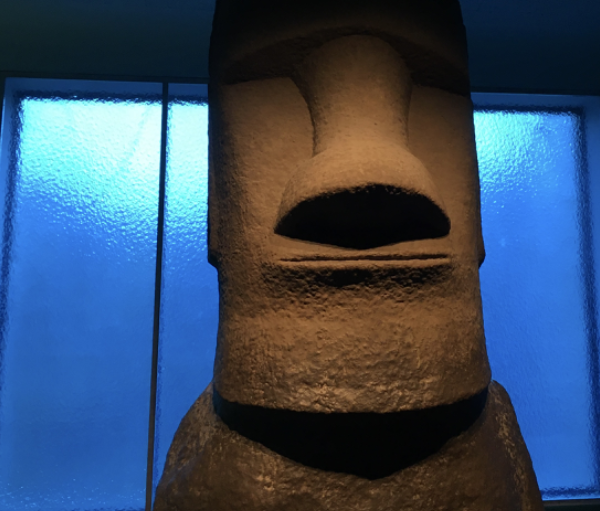 Statue moai en pierre, tête stylisée avec un nez proéminent et une expression neutre, exposée dans un musée.