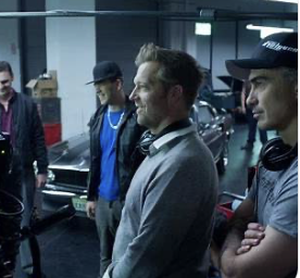 Un groupe de professionnels en studio, discutant autour d'un véhicule. Trois hommes portent des casquettes et accessoires de