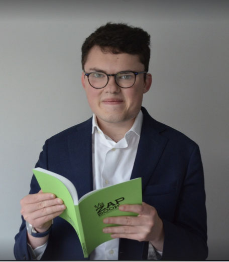 Homme en costume tenant un livre vert avec texte "APEC" et "2020" en arrière-plan neutre