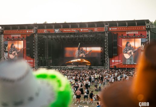 Concert en plein air sur scène Carorock avec foule et effets pyrotechniques, artistes jouant de la guitare sur écrans géan
