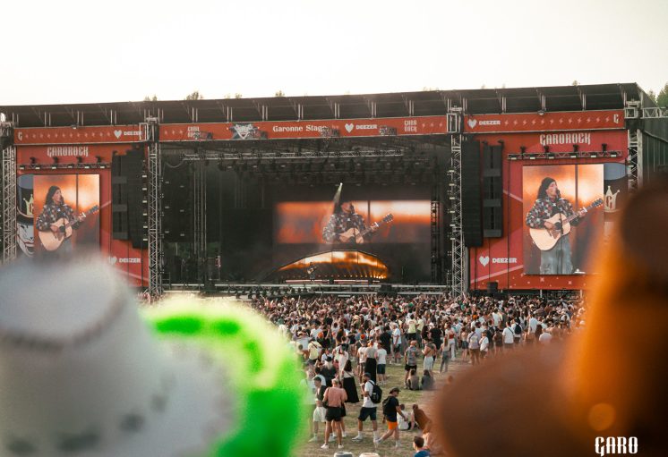 Concert en plein air sur scène Carorock avec foule et effets pyrotechniques, artistes jouant de la guitare sur écrans géan