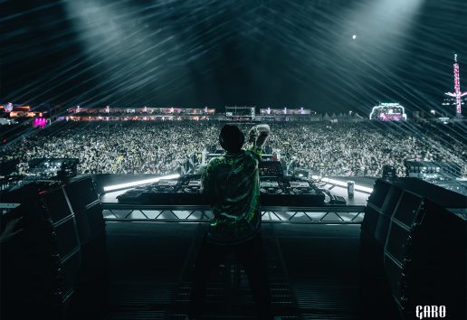 Un DJ sur scène avec des platines, entouré de milliers de spectateurs lors d’un concert nocturne sous éclairage dynamiqu