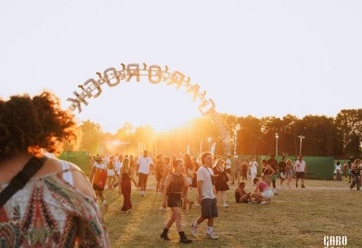 Foule en extérieur lors d’un événement musical au coucher de soleil avec un grand arch surplombant l’entrée indiquant